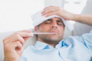 Sick man lying on sofa checking his temperature