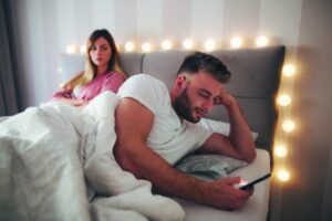 Man typing text message on phone and his girlfriend is angry because of that.