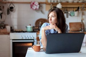 Working from home office. Upset woman using laptop and Internet. Freelancer workplace at kitchen table.