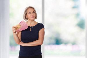 Attractive middle aged woman relaxing with fan. Mature woman experiencing hot flush from menopause