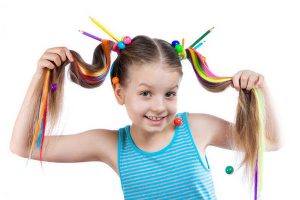 Portrait of a funny girl with colorful strands in her hair. Color pencils, beads, colored strands of hair in the hair.