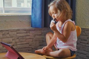 Little cute child girl watching something in the tablet and eats fruit bar