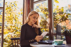 Beautiful blond woman using her smart-phone and relaxing in cafe surrounded by nature.