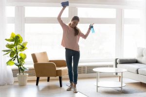 Cheerful woman makes house cleaning holding rag spray bottle detergent