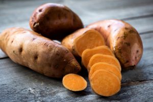 Raw sweet potatoes on wooden background closeup