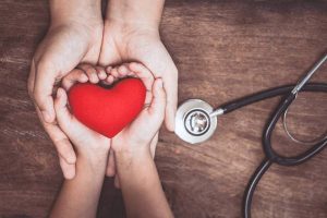 Red heart on woman and child hands and with doctor's stethoscope on wooden background