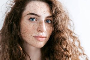 Beautiful Freckles young woman close up portrait. Attractive model with beautiful blue eyes and ginger curly hair