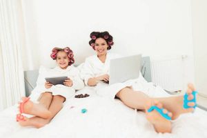 Mom and little daughter are lying on the bed in white bathrobes in the bedroom.