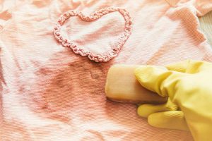 Removing stains with bile( gall, sap) soap bar. Natural chemical free household clothing washing products concept. Hand holding soap bar and rubbing removing stain from pink blouse.