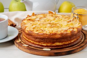 Cheesecake, apple pie, curd dessert with polenta, apples, almond flakes and cinnamon on white marble kitchen table, side view
