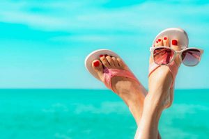 Upside woman feet and red pedicure wearing pink sandals, sunglasses at seaside. Funny and happy fashion young woman relax on vacation. Chill out girl at beach. Creative for tour agent. Weekend travel.