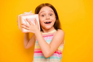 Portrait of lovely child holding present for 8-march screaming wow omg isolated over yellow background