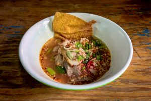 Thai spicy rice noodles in pork soup, fried dumpling, peanut and vegetable on old wooden background