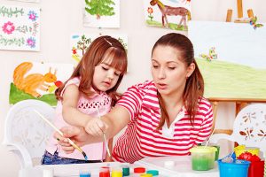 Child with teacher draw paints in play room. Preschool.
