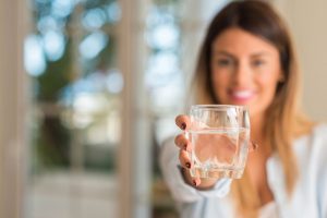 Beautiful young woman smiling while holding a glass of water at home. Lifestyle concept.