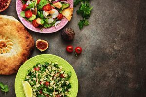 Middle Eastern salads tabbouleh and fattoush, pitta bread, pomegranate, figs on a dark rustic background. Arabic dishes, top view.