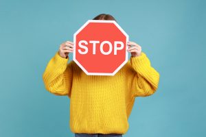 Portrait of unknown little kid covers face with Stop symbol, anonymous child holds red traffic sign.