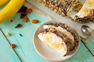 Dessert of cottage cheese cream, banana and chocolate frosting with nuts on a festive table.