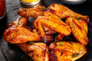 Buffalo chicken wings with a cheese sauce and a glass of beer on a dark background
