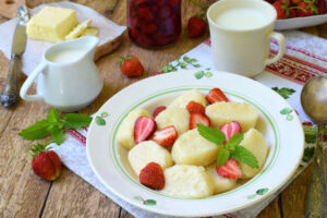 Summer berry breakfast. Sweet lazy pierogi, dumplings with sour cream, butter and strawberry on wooden background. Italian gnocchi. Copy space for your text.
