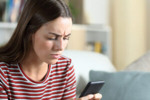 Annoyed,Woman,Checking,Smart,Phone,Sitting,On,A,Sofa,In