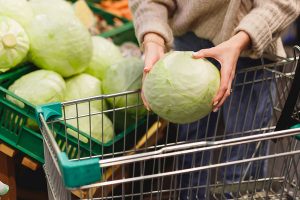 Woman,Puts,Head,Of,Fresh,Young,Cabbage,In,Shopping,Trolley