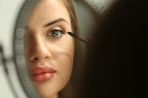 Beautiful young woman looking in mirror while applying makeup